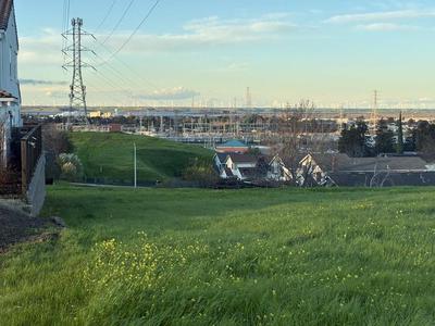 Looking north along a high voltage transmission line, new substation in the foreground, and windmills across the Delta. Just out of frame is the BART transit stop with rooftop solar arrays over the parking lot, and multiple pollution towers to the east. Antioch, CA 2025.